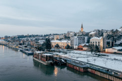 An illustrative photo of city buildings covered in snow near a body of water.