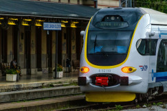 An illustrative photo of a white and blue train traveling past a train station.