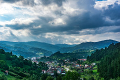 An illustrative photo of houses in the mountains with green pine trees.