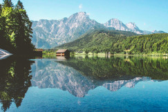 An illustrative photo of a house near a lake and mountains.
