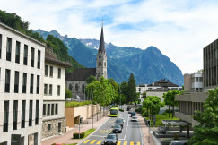 An illustrative photo of cars on a road in a town with mountains in the background.