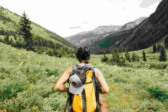 An illustrative photo of a person carrying yellow and black backpack walking in the mountains.