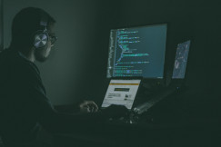 An illustrative photo of a person using a computer and a laptop.