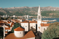 An illustrative photo of buildings near a lake and mountains.