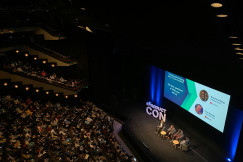 An illustrative photo of people sitting in a big hall looking at a screen.