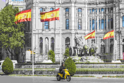 An illustrativephoto of a man riding a motorcycle near a white building.