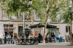 An illustrative photo of a group of people sitting at a table under an umbrella in Spain.