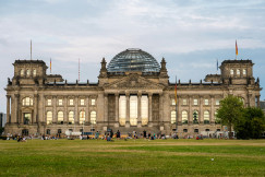 An illustrative photo of people sitting on grass near a large building with a dome.