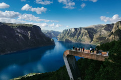 An illustrative photo of people standing on bridge looking through mountain surrounded by water.