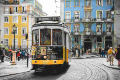 An illustrative photo of a yellow and white tram on road near white concrete building.