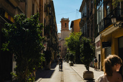 An illustrative photo of a man riding a bicycle on a narrow street surrounded by buildings.