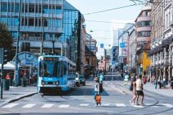 An illustrative photo of a blue bus driving down a street next to tall buildings.