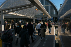 An illustrative photo of a group of people walking down a sidewalk next to a train station.