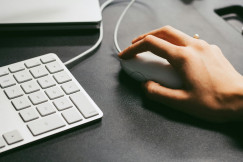 Hand using a computer mouse beside a keyboard on a desk.
