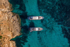 An illustrative photo of two white boats in a body of water near a rocky shore.