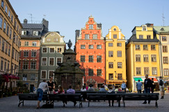 An illustrative photo of people sitting on a bench near buildings of different colours.