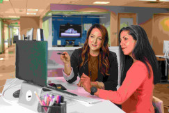 An illustrative photo of two women sitting at a table looking at a computer screen.