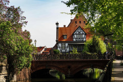 An illustrative photo of a bridge over a river with a house in the background.