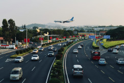An illustrative photo of a large airplane flying over a busy highway.