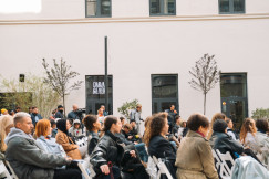 Audience seated outdoors at an event in a courtyard, listening attentively during a public talk or presentation.
