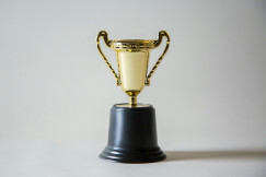 Gold trophy cup with handles on a black base against a plain background.