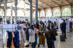 Indoor fashion exhibition with clothing racks and attendees browsing.