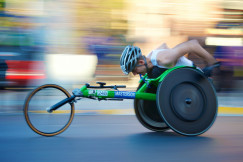 Wheelchair athlete speeding forward in a road race, with a motion blurred background.