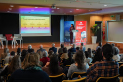Speaker presenting to an audience in a conference hall.