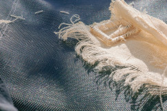 Close up of ripped denim fabric with frayed threads.
