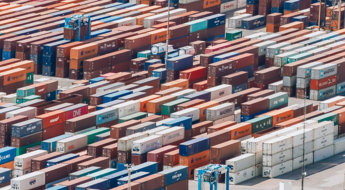 Aerial view of a large container terminal with hundreds of stacked shipping containers and transport vehicles, representing global logistics and international trade.
