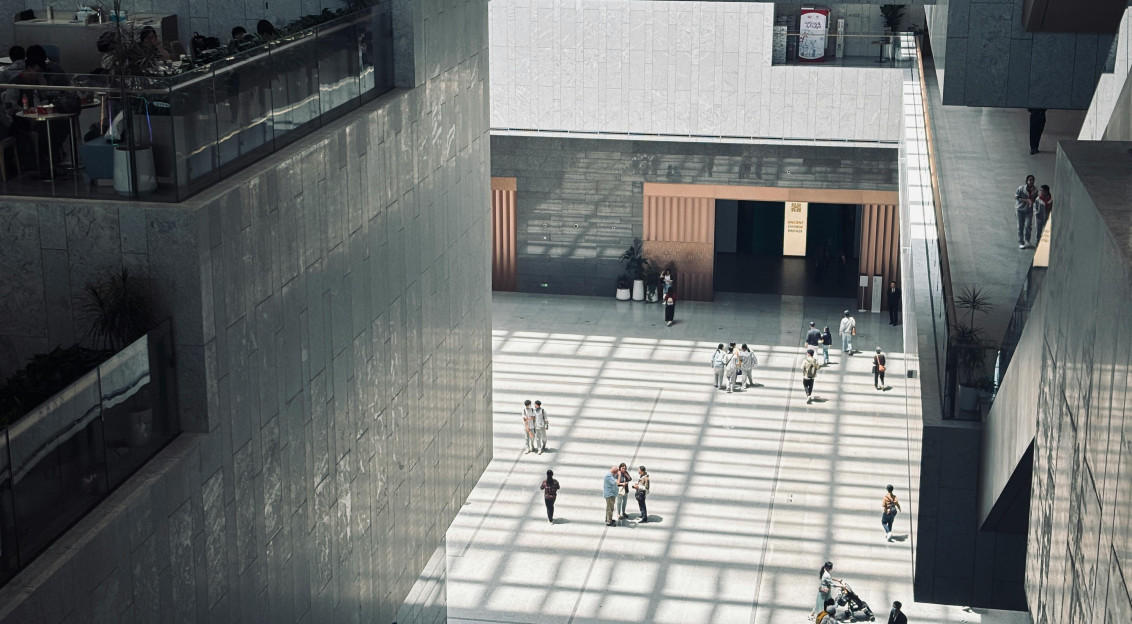 A spacious indoor atrium with geometric shadows and people walking by.