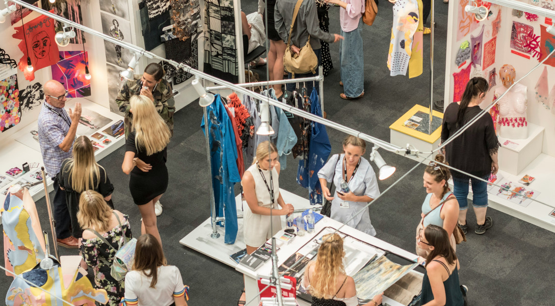 Textile exhibition booth with visitors browsing garments, artwork, and fabric displays.