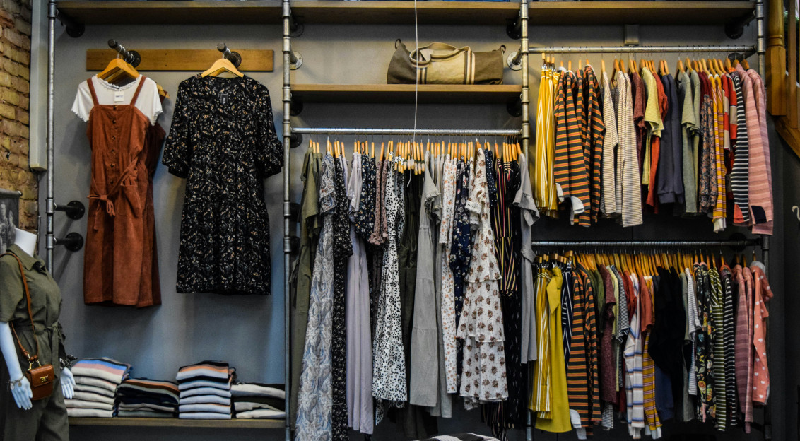 Clothing displayed on racks and shelves inside a fashion store, illustrating themes of fashion consumption, retail and alternative approaches to sustainable fashion.