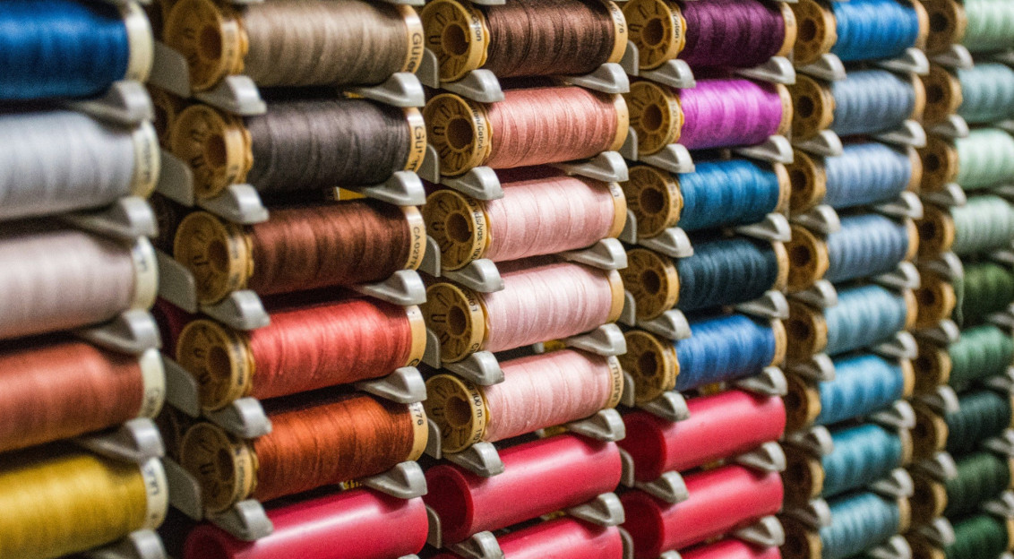 Close up view of multiple colourful thread spools arranged on shelves, representing textile manufacturing, yarn production and material diversity within the textile industry.