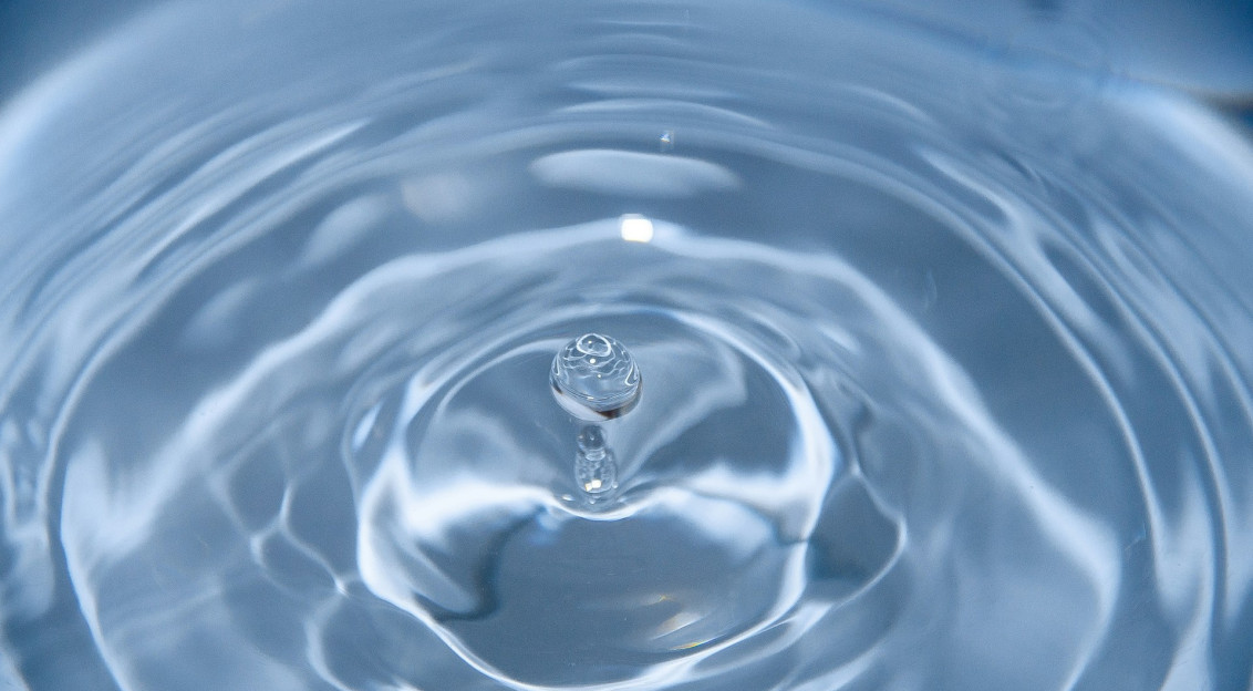 A photo presenting a droplet rebounding from a rippling blue water surface, captured in macro detail.