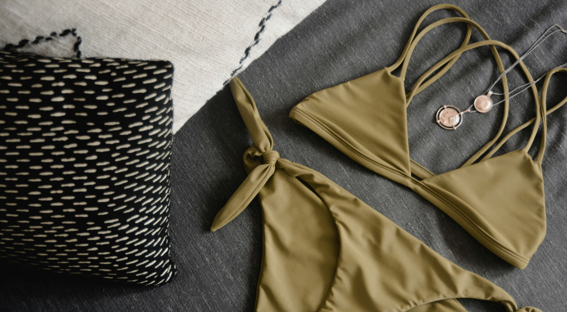 Modern olive green bikini set with matching accessories displayed on a dark fabric surface, representing contemporary swimwear design and fashion textiles.