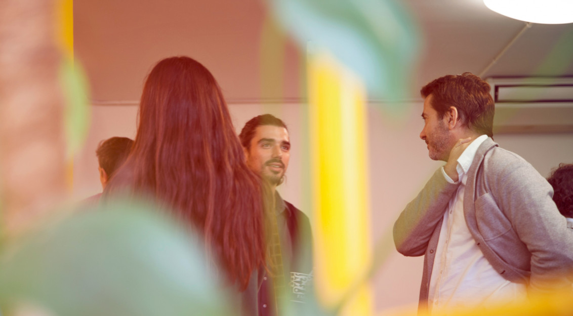 A photo presents people talking during an indoor meeting.