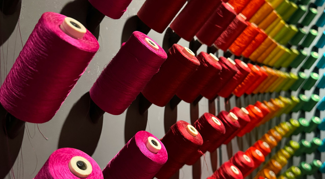 Rows of colourful textile yarn spools displayed on a wall, representing textile production, material innovation and the fashion and lifestyle industries.