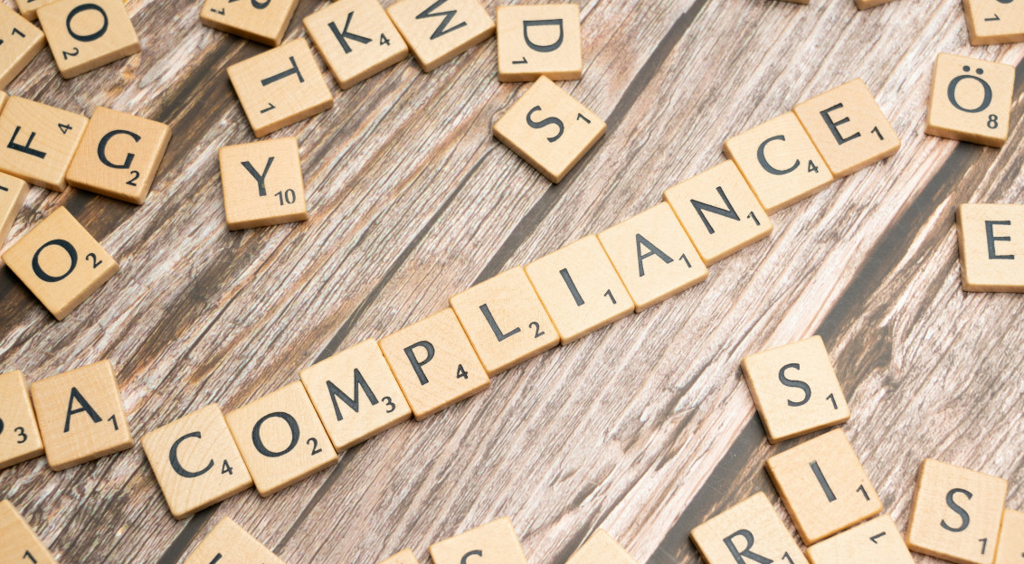 Photo presenting wooden letter tiles arranged on a rustic wooden surface, with the word “COMPLIANCE”
