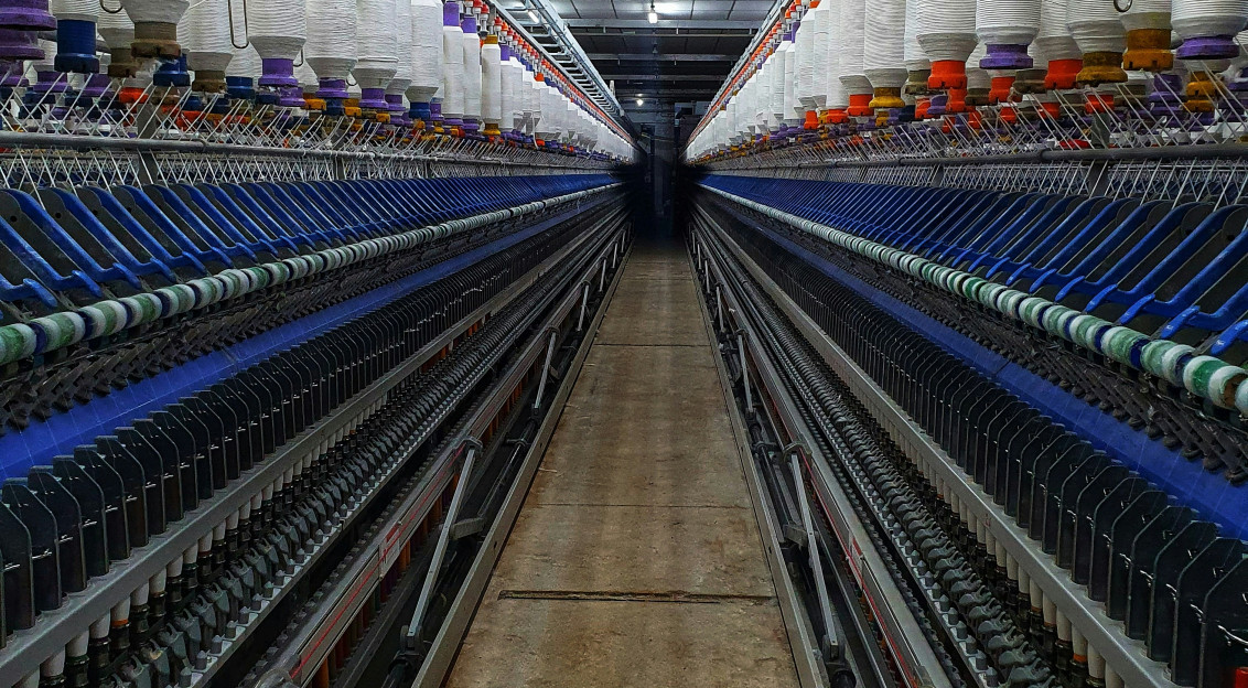 Industrial textile spinning machines with rows of yarn spools in a manufacturing facility, representing textile production, material innovation and sustainable industrial transformation.