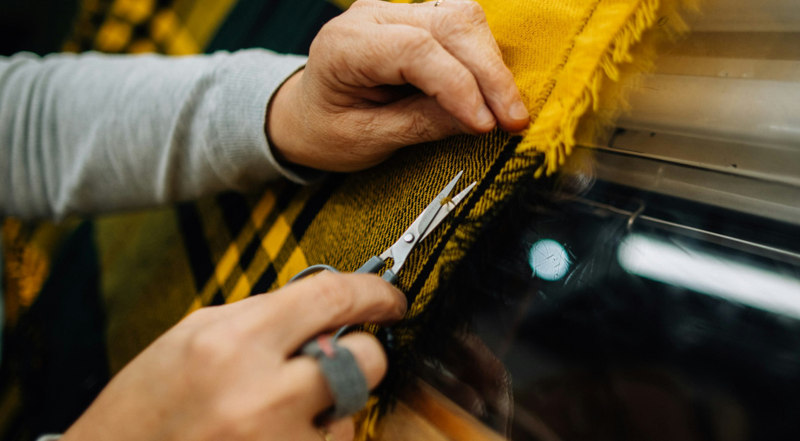 Close up of hands inspecting and trimming a woven textile fabric, demonstrating textile quality control, craftsmanship and material evaluation during fabric production.