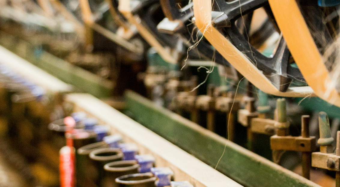 Close-up of textile manufacturing machinery processing yarn in an industrial spinning facility, representing textile engineering, material performance and research into durable textile products.
