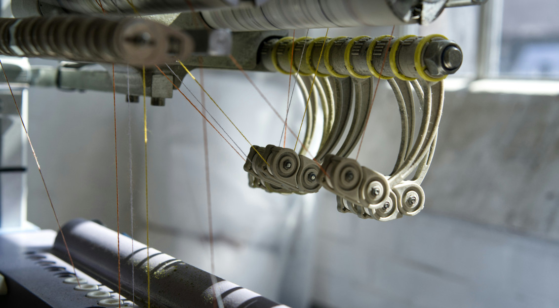 Close up of an industrial textile machine processing multiple yarns, illustrating advanced manufacturing technologies used in the production of smart and functional textiles.