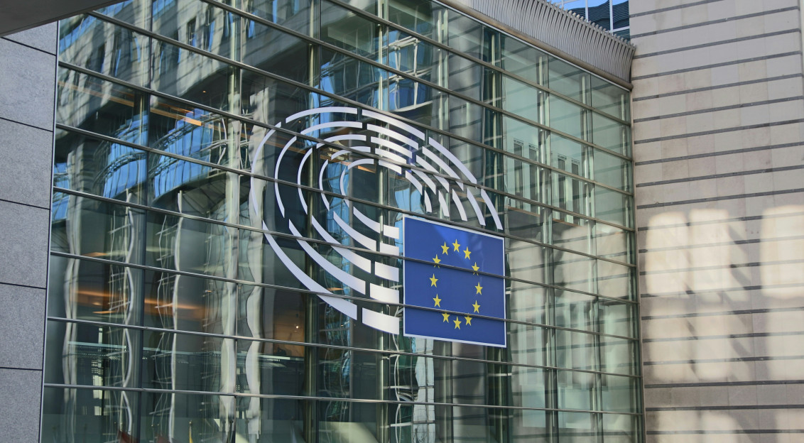 European Parliament logo and EU flag displayed on the glass facade of a building.