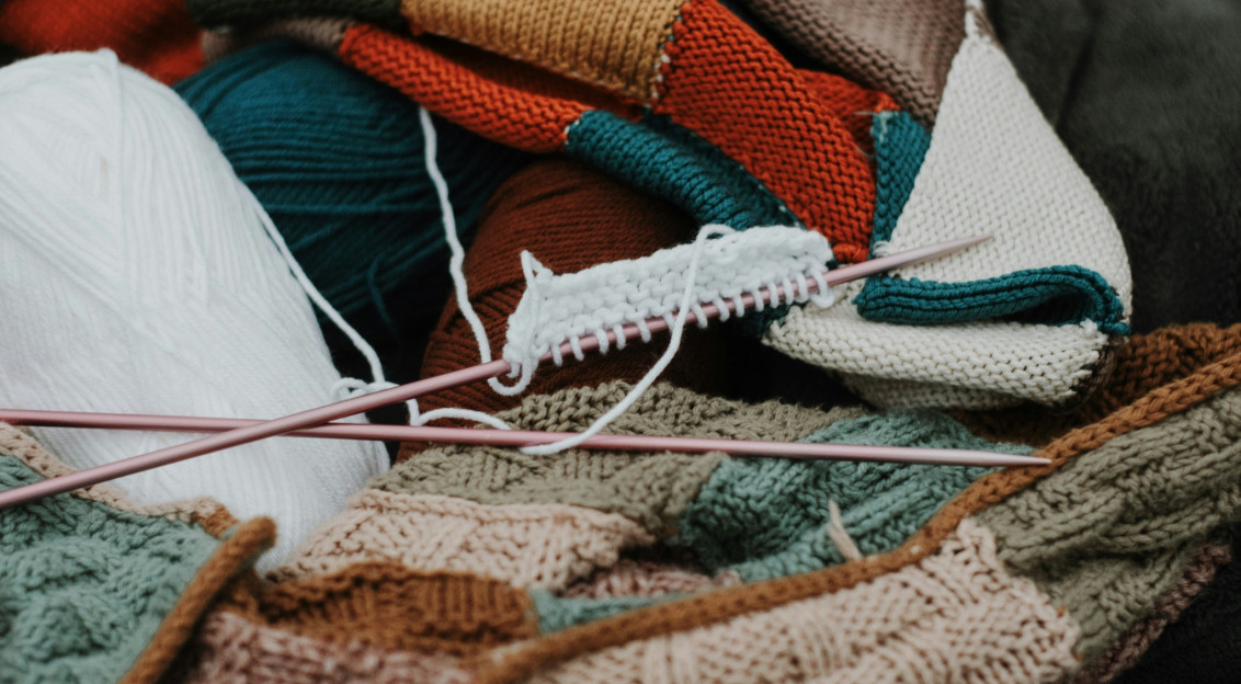 Colourful yarn, knitted textiles and knitting needles representing textile crafts and creative production.