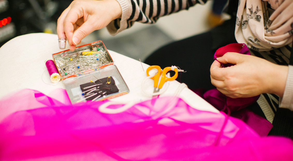 Person working with bright pink fabric alongside sewing needles, thread and scissors.
