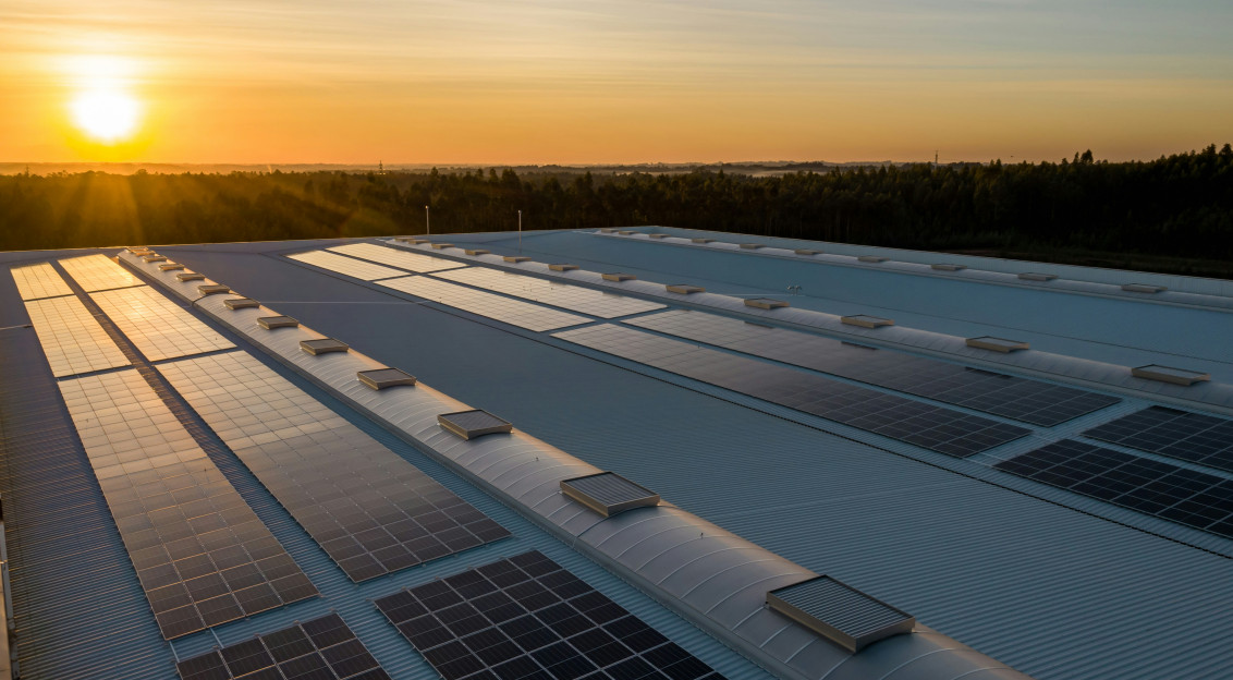 The photo presents solar panels on a large roof at sunset.