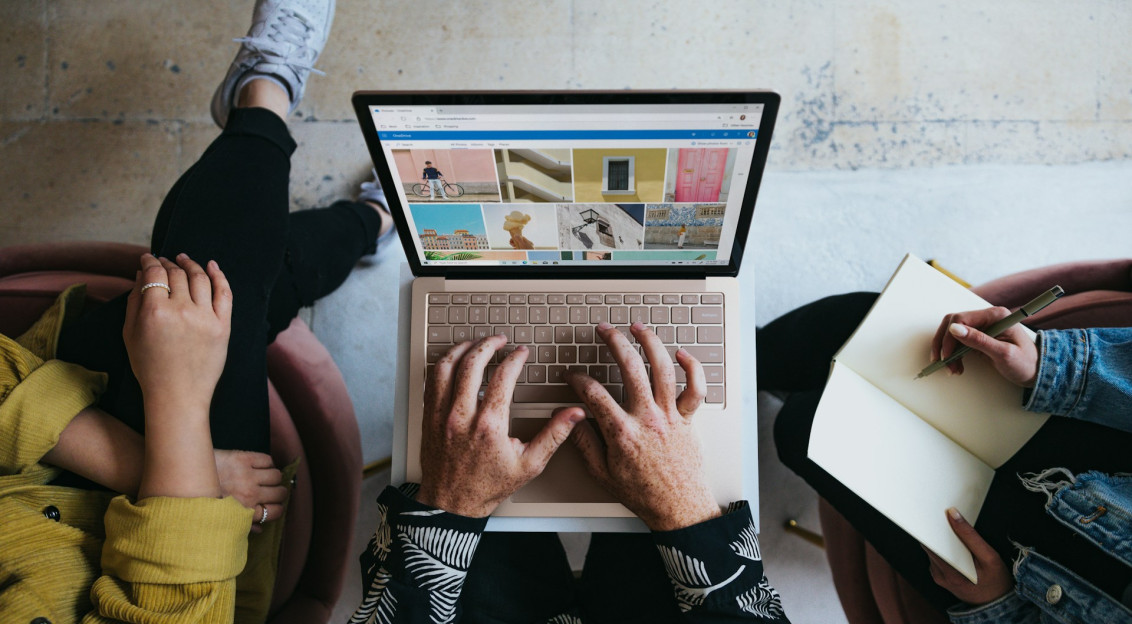 The photo presents people collaborating on a laptop while taking notes.