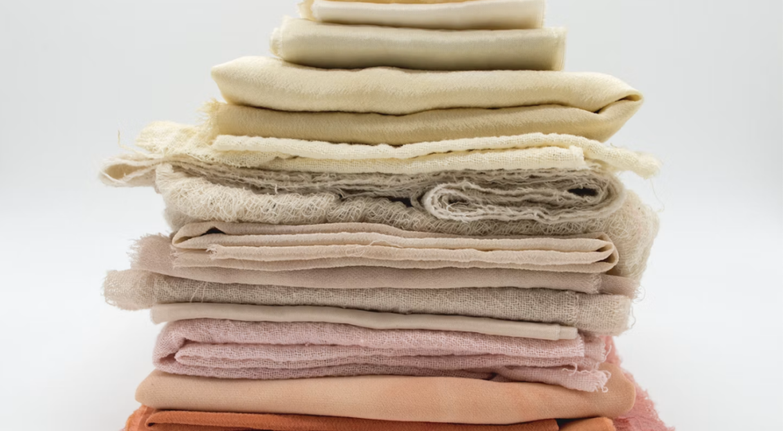 Stack of folded fabrics in pink, red, yellow, grey, and brown on a white surface. 