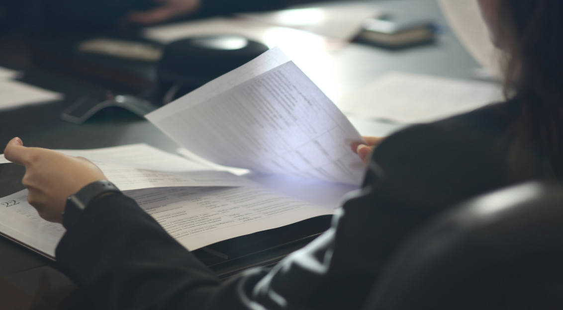 The picture describes a person sitting at a table and reviewing printed documents.